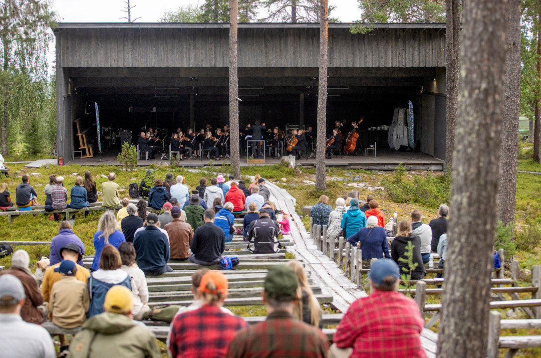 Joukko ihmisiä kuuntelee orkesteria soittoa ulkona