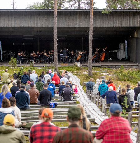 Joukko ihmisiä kuuntelee orkesteria soittoa ulkona