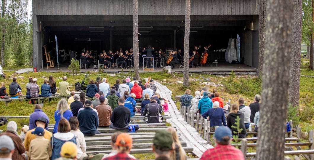 Joukko ihmisiä kuuntelee orkesteria soittoa ulkona